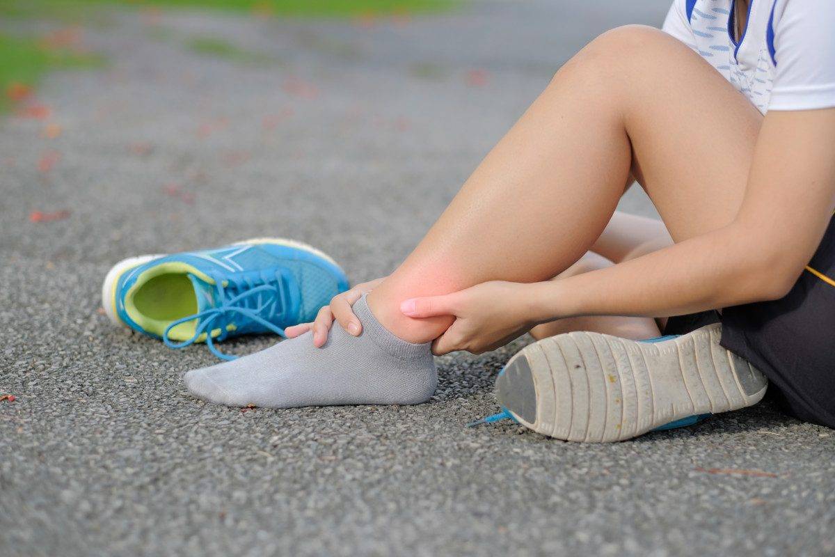 Young fitness woman holding his sports leg injury, muscle painful during training. Asian runner having knee ache and problem after running and exercise outside in summer