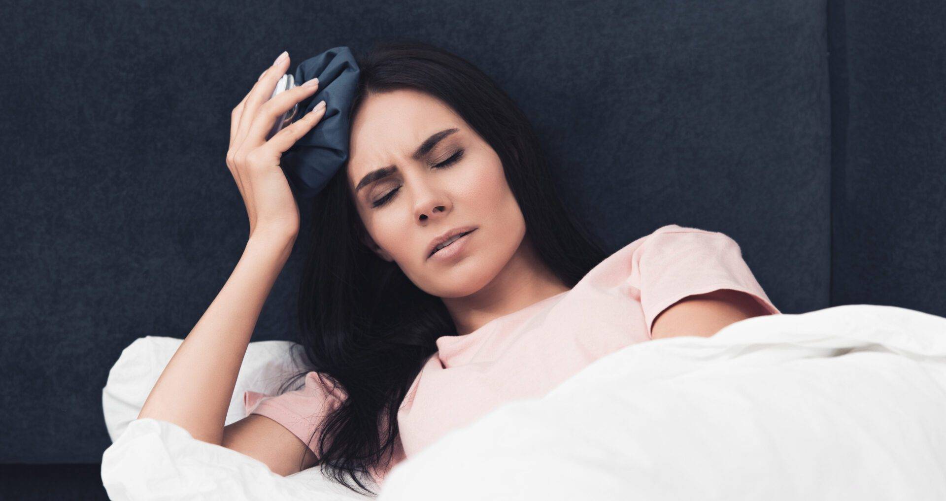 suffering sick young woman holding ice pack on head while lying in bed