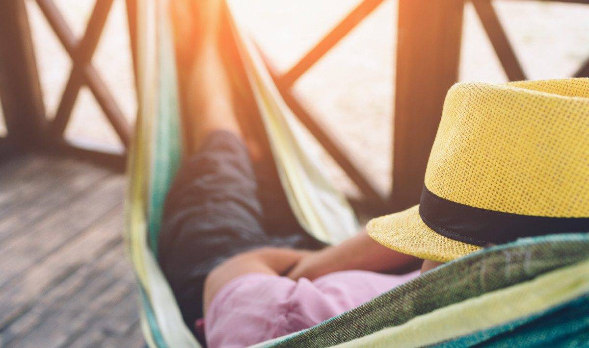 Young man lying in hammock at sunny beach by ocean and sleeping. He hold had on face. Young man chilling.