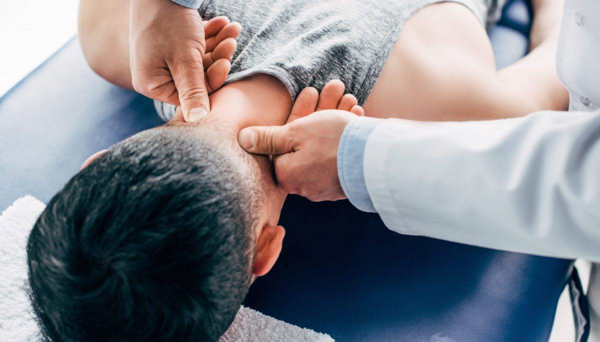 chiropractor massaging neck of man lying on Massage Table with towel