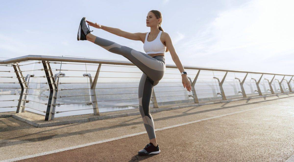 Sportive lady doing leg swing on foot bridge